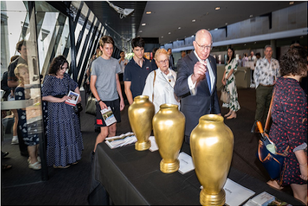 Audience members gathered around three golden voting urns in a theatre foyer